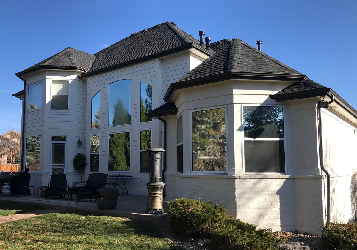 Dark gutters and downspouts on a white two-story house — photo from the Quality Pro Raingutters page